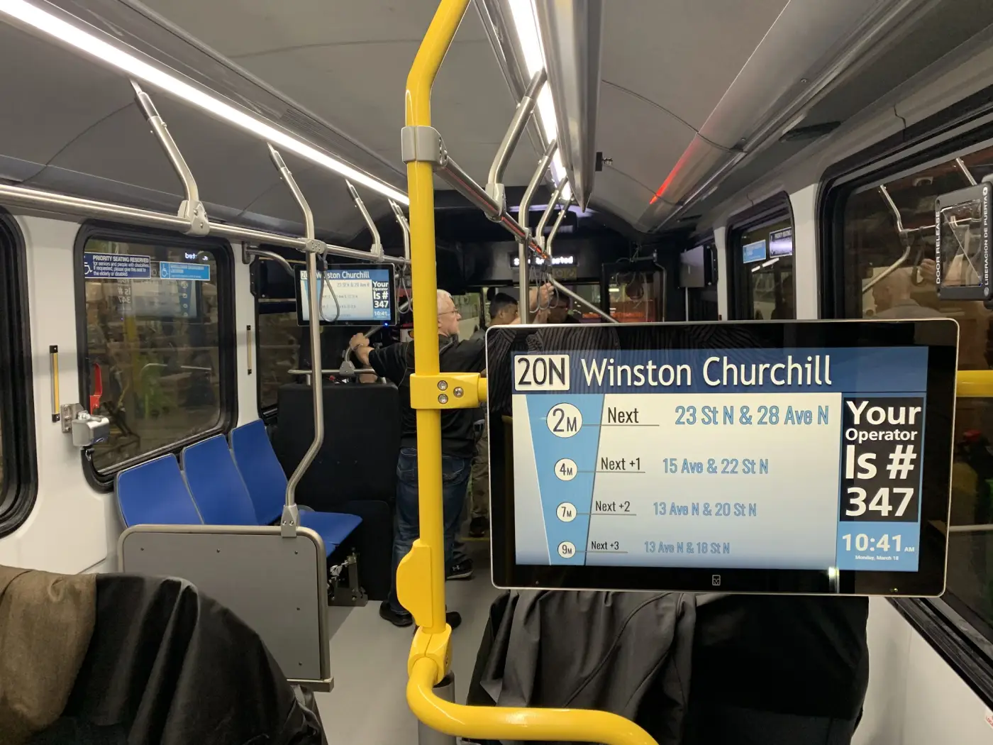 A superwide onboard display calling the next stop above the aisle, in revenue service.