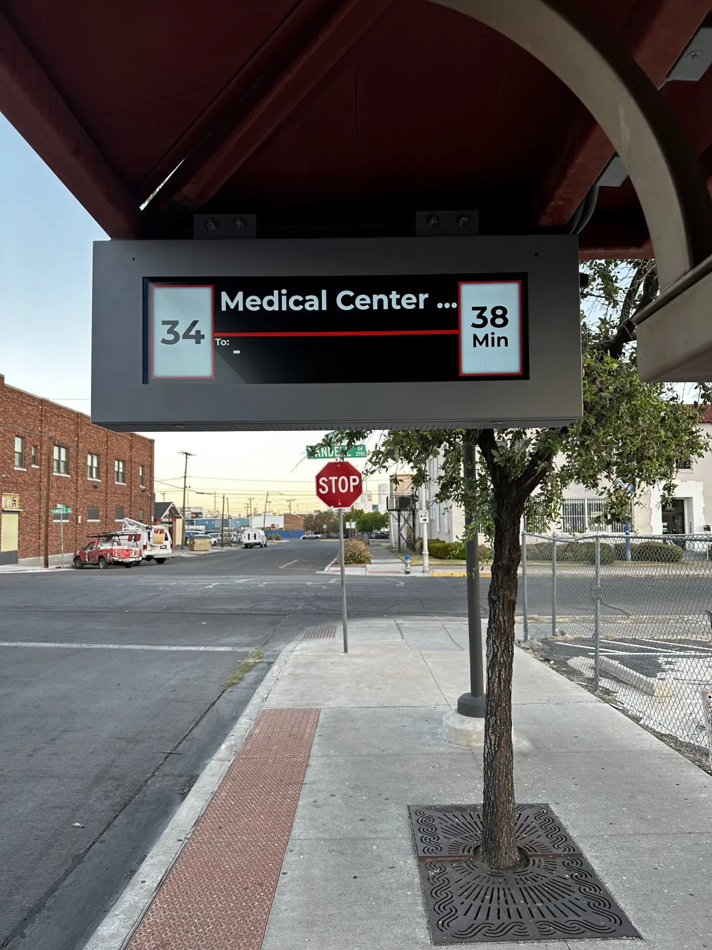 Overhead next-arrival display mounted under a shelter canopy showing route 34 to Medical Center in 38 minutes